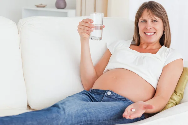 Wunderschöne schwangere Frau nimmt eine Pille, während sie auf einem Sofa liegt — Stockfoto