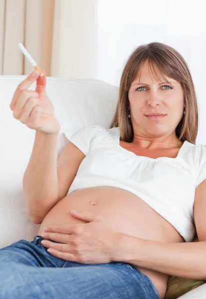 Preciosa mujer embarazada sosteniendo un cigarrillo mientras está acostada en un sofá — Foto de Stock