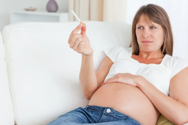 Красивая беременная женщина держит сигарету, пока лежит на так — стоковое фото