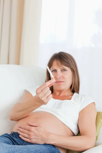 Mujer embarazada de buen aspecto sosteniendo un cigarrillo mientras está acostado en un —  Fotos de Stock