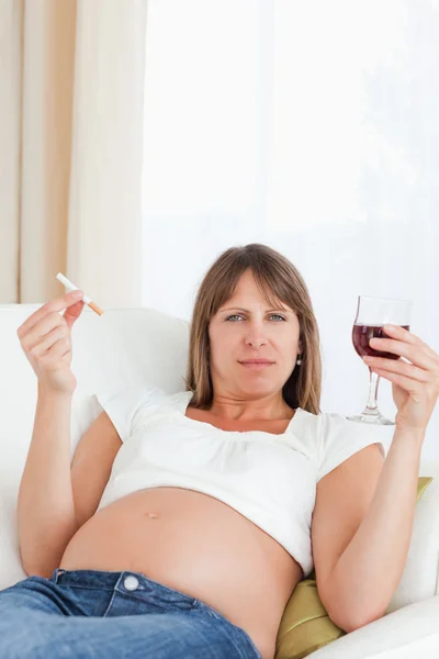 Hermosa mujer embarazada sosteniendo un cigarrillo y un vaso de rojo — Foto de Stock