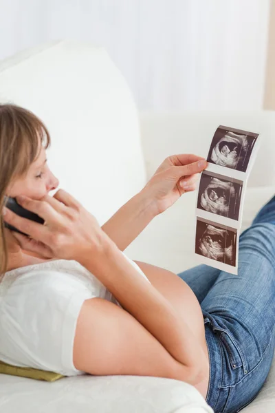 Mulher grávida bonita no telefone e olhando para um ultra-som — Fotografia de Stock