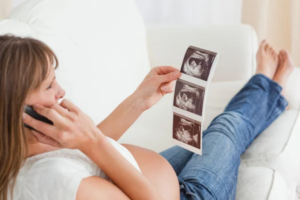 Приваблива вагітна жінка по телефону і дивиться на ультразвук — стокове фото
