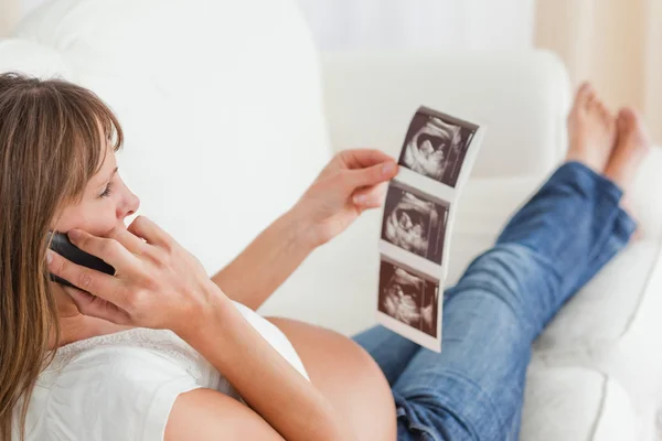 Gut aussehende schwangere Frau am Telefon und Blick auf ein Ultra — Stockfoto