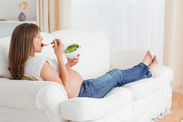 Jolie femme enceinte mangeant une salade allongée sur un canapé — Photo