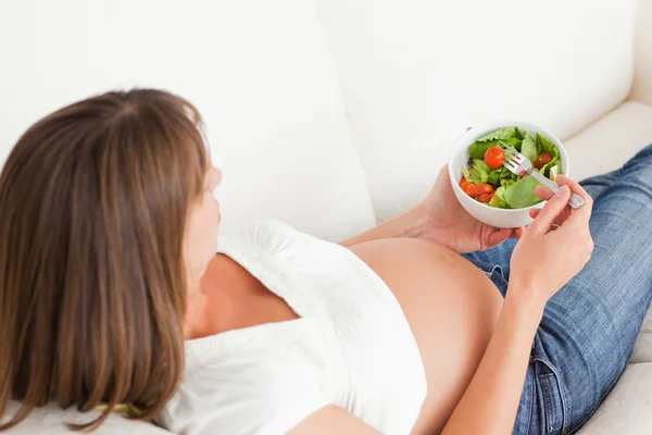魅力的な妊娠中の女性はソファーの上に横たわっている間、サラダを食べる — ストック写真