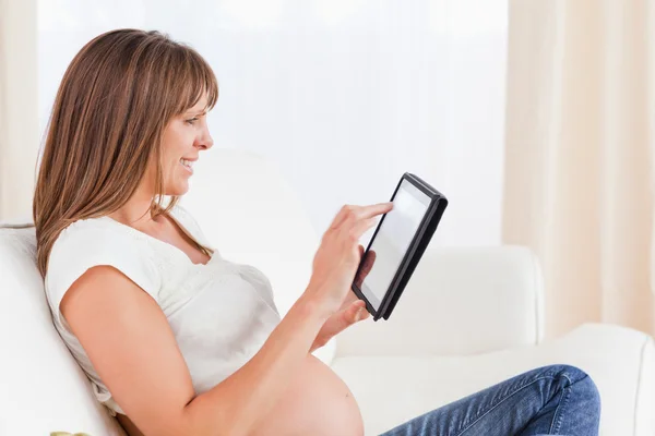 Krásná těhotná žena relaxační s počítačem tablet zároveň s — Stock fotografie