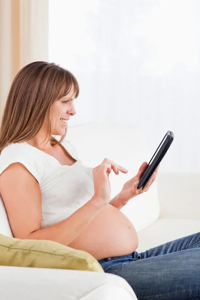 Atractiva mujer embarazada relajándose con una tableta de computadora mientras — Foto de Stock