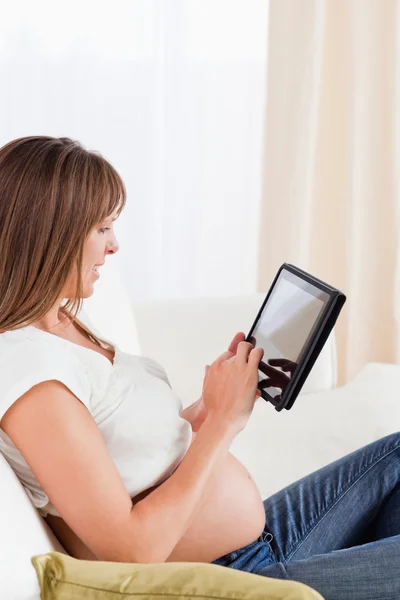 Mulher grávida bonita relaxando com um tablet de computador enquanto — Fotografia de Stock