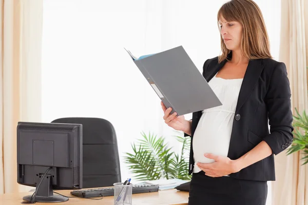 Hermosa hembra embarazada sosteniendo un archivo mientras está de pie — Foto de Stock
