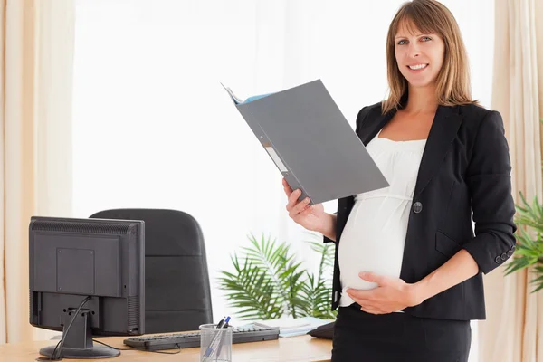 Привлекательная беременная женщина держит папку, стоя — стоковое фото