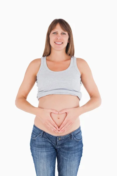 Linda fêmea grávida posando enquanto forma um coração com seu han — Fotografia de Stock