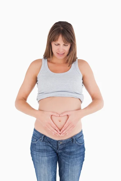Atractiva hembra embarazada posando mientras forma un corazón con ella —  Fotos de Stock