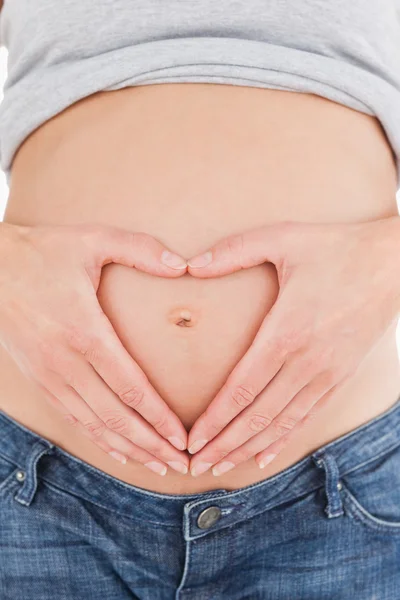 Primer plano de una mujer embarazada posando mientras forma un corazón con —  Fotos de Stock