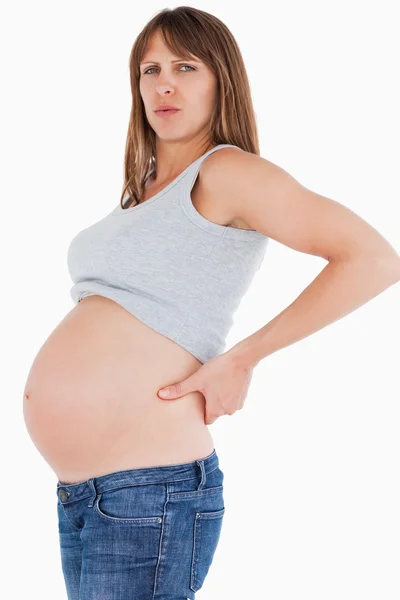 Mulher grávida de boa aparência segurando suas costas enquanto em pé — Fotografia de Stock