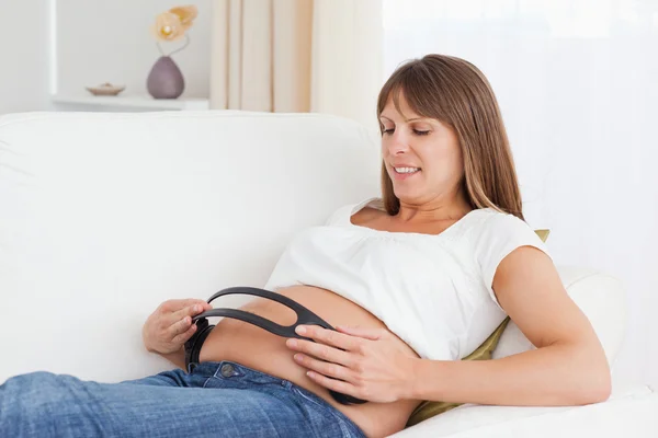 Närbild på en gravid kvinna med hörlurar på hennes mage — Stockfoto