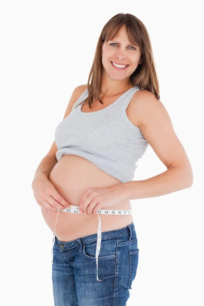 Hermosa mujer embarazada midiendo su vientre mientras está de pie —  Fotos de Stock