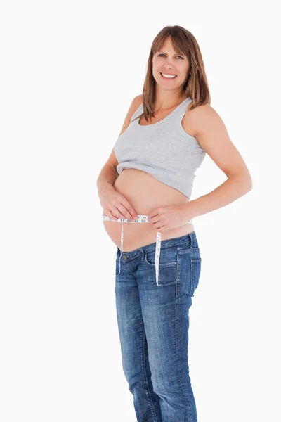 Bonne femme enceinte loooking mesurant son ventre tout en se tenant debout — Photo