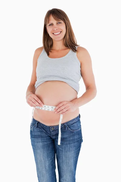 Linda mujer embarazada midiendo su vientre mientras está de pie —  Fotos de Stock