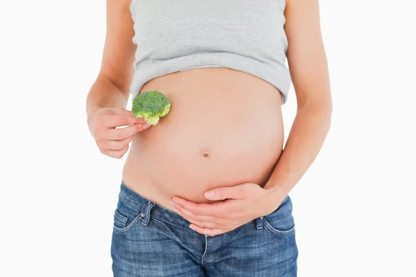 Mulher grávida segurando um brócolis enquanto em pé — Fotografia de Stock