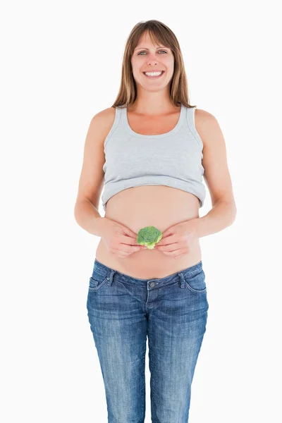 Mulher grávida bonita segurando um brócolis enquanto está de pé — Fotografia de Stock