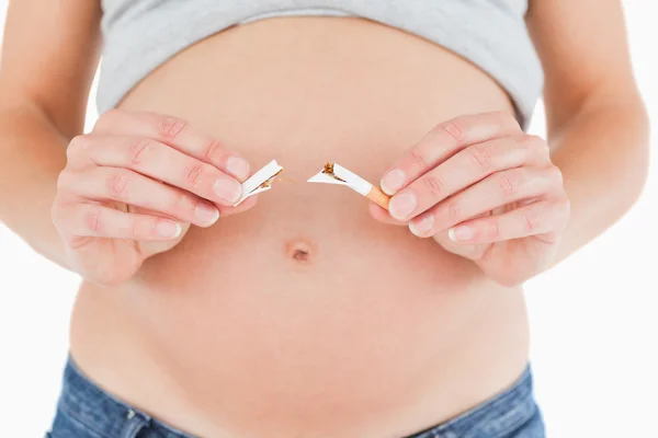 Νεαρή έγκυο γυναίκα, κρατώντας ένα σπασμένο τσιγάρο ενώ στέκεται — Φωτογραφία Αρχείου
