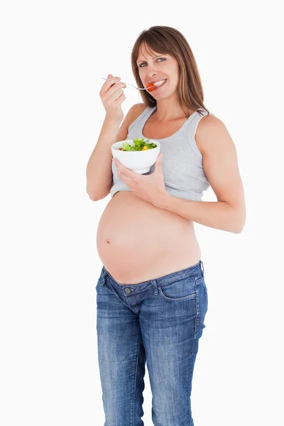 Atractiva mujer embarazada comiendo un tomate cereza mientras sostiene un —  Fotos de Stock