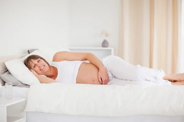 Mulher grávida atraente relaxando enquanto deitada em sua cama — Fotografia de Stock