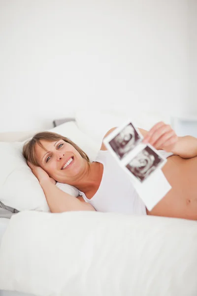 Hermosa mujer embarazada sosteniendo una ecografía mientras está acostada —  Fotos de Stock