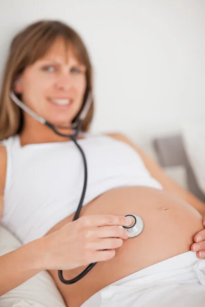 Krásná těhotná žena pomocí stetoskopu vleže na posteli — Stock fotografie