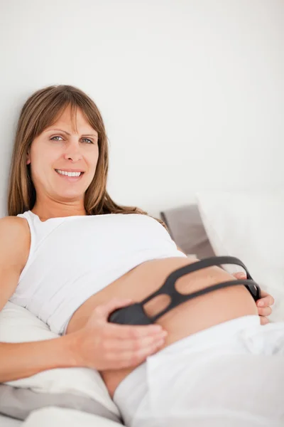 Mulher grávida bonita usando fones de ouvido enquanto deitada em uma cama — Fotografia de Stock