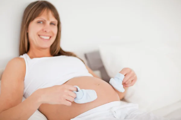 Mulher grávida atraente brincando com meias pequenas enquanto deitado — Fotografia de Stock