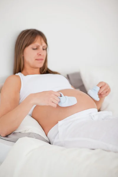 Mulher muito grávida brincando com meias pequenas enquanto deitado em um — Fotografia de Stock