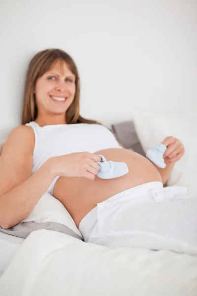 Encantadora mujer embarazada jugando con pequeños calcetines mientras está acostada —  Fotos de Stock