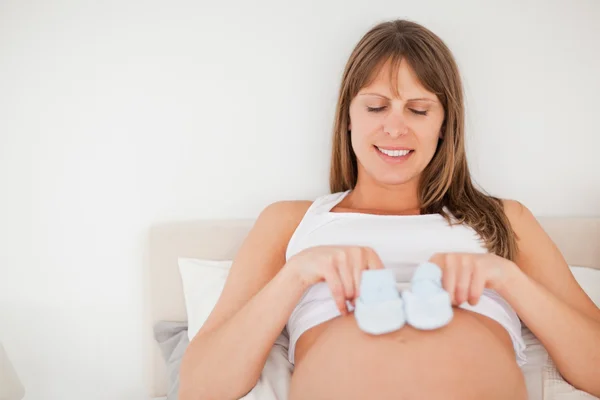 Preciosa mujer embarazada jugando con calcetines pequeños mientras está acostada en un — Foto de Stock