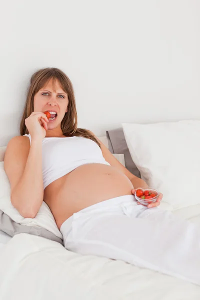 Bella femmina incinta mangiare alcune fragole mentre lyin — Foto Stock