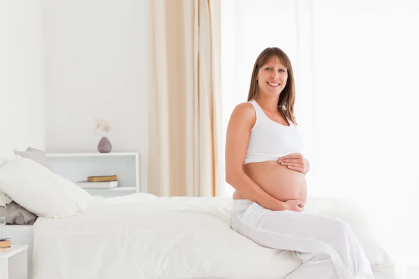 Yatağı üzerinde otururken poz güzel hamile kadın — Stok fotoğraf