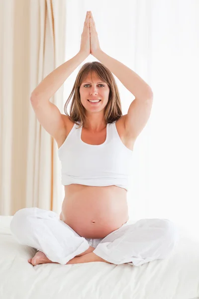 Aantrekkelijke zwangere vrouw doet yoga op een bed — Stockfoto