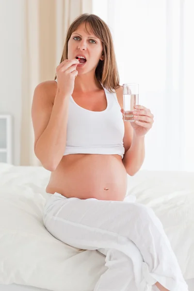 Όμορφη έγκυο γυναίκα, λαμβάνοντας ένα χάπι, ενώ κάθεται σε ένα κρεβάτι — Φωτογραφία Αρχείου