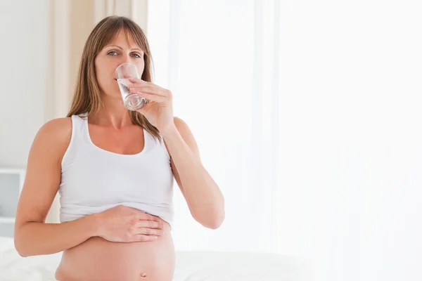 Niedliche schwangere Frau nimmt eine Pille, während sie auf einem Bett sitzt — Stockfoto