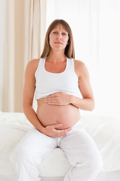 Roztomilý těhotná žena hladí její břicho, zatímco sedí na posteli — Stock fotografie