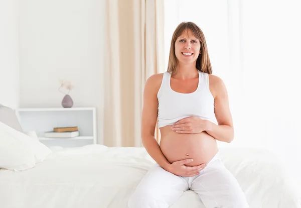 Красивая беременная женщина ласкает живот, сидя на — стоковое фото