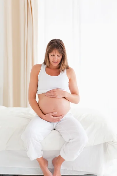 Bien parecido embarazada hembra acariciando su vientre mientras está sentado o —  Fotos de Stock