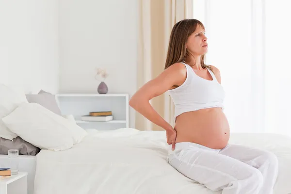 Беременная женщина испытывает боли в спине, сидя на диване — стоковое фото