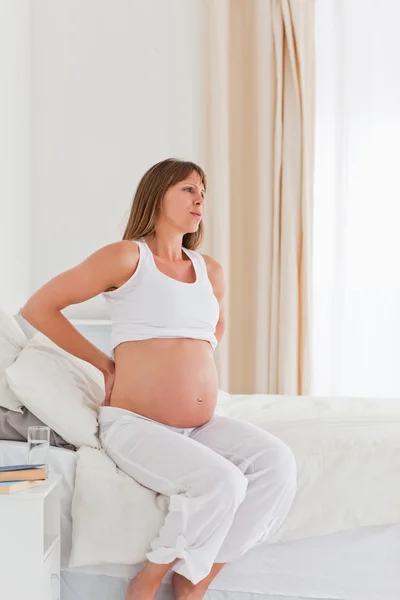 Очаровательная беременная женщина, испытывающая боль в спине, сидя на диване — стоковое фото