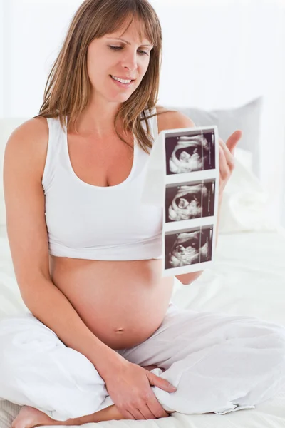Encantadora hembra embarazada mostrando una ecografía mientras está sentada —  Fotos de Stock