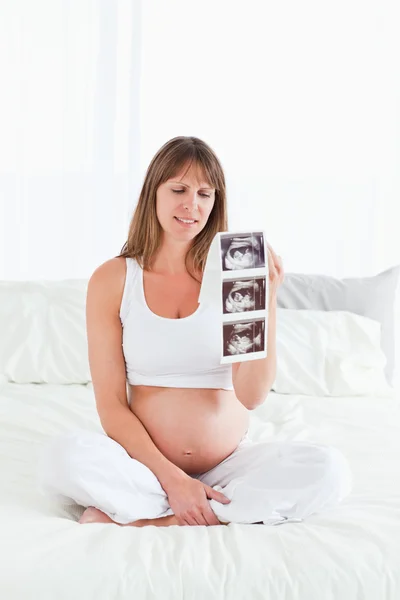 Mujer bastante embarazada mostrando una ecografía mientras está sentada — Foto de Stock