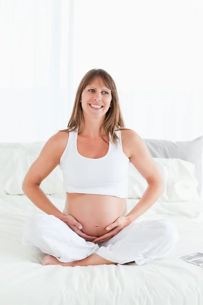 Беременная женщина позирует, сидя на кровати — стоковое фото