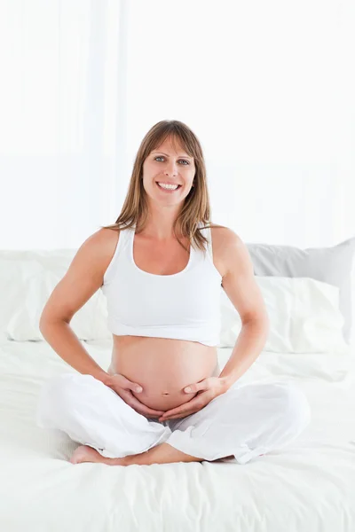 Красивая беременная женщина позирует, сидя на кровати — стоковое фото