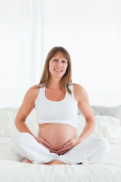 Atraente fêmea grávida posando enquanto sentado em uma cama — Fotografia de Stock
